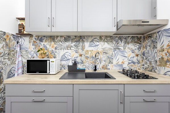 A kitchen with a microwave, sink, and stove, with a floral backsplash and grey cabinets.