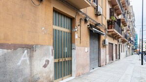 A narrow urban street with buildings featuring balconies, some with plants, and a closed shop with a metal shutter. - Apartment 'La Dimora Di Elma' with Wi-Fi and Air Conditioning (Palermo)