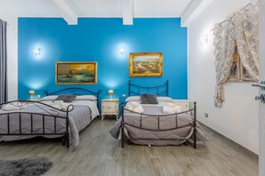 A room with two beds, a blue wall, and a painting.