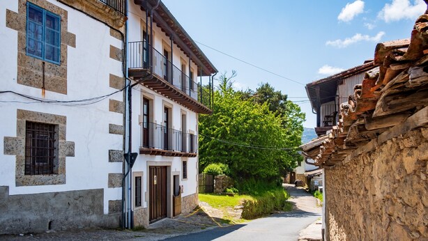 A narrow street with traditional buildings, a stone wall on one side, and a clear sky.