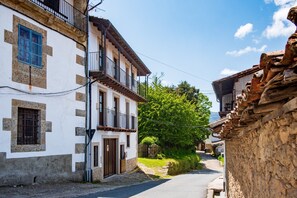 A narrow street with traditional buildings, a stone wall on one side, and a clear sky.