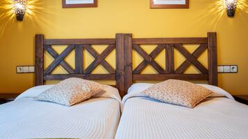 Een tweepersoonsbed met een houten hoofdbord, twee kussens, een groene plaid en twee wandlampen.