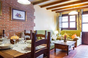 A dining area with a brick wall, wooden furniture, and a green sofa.