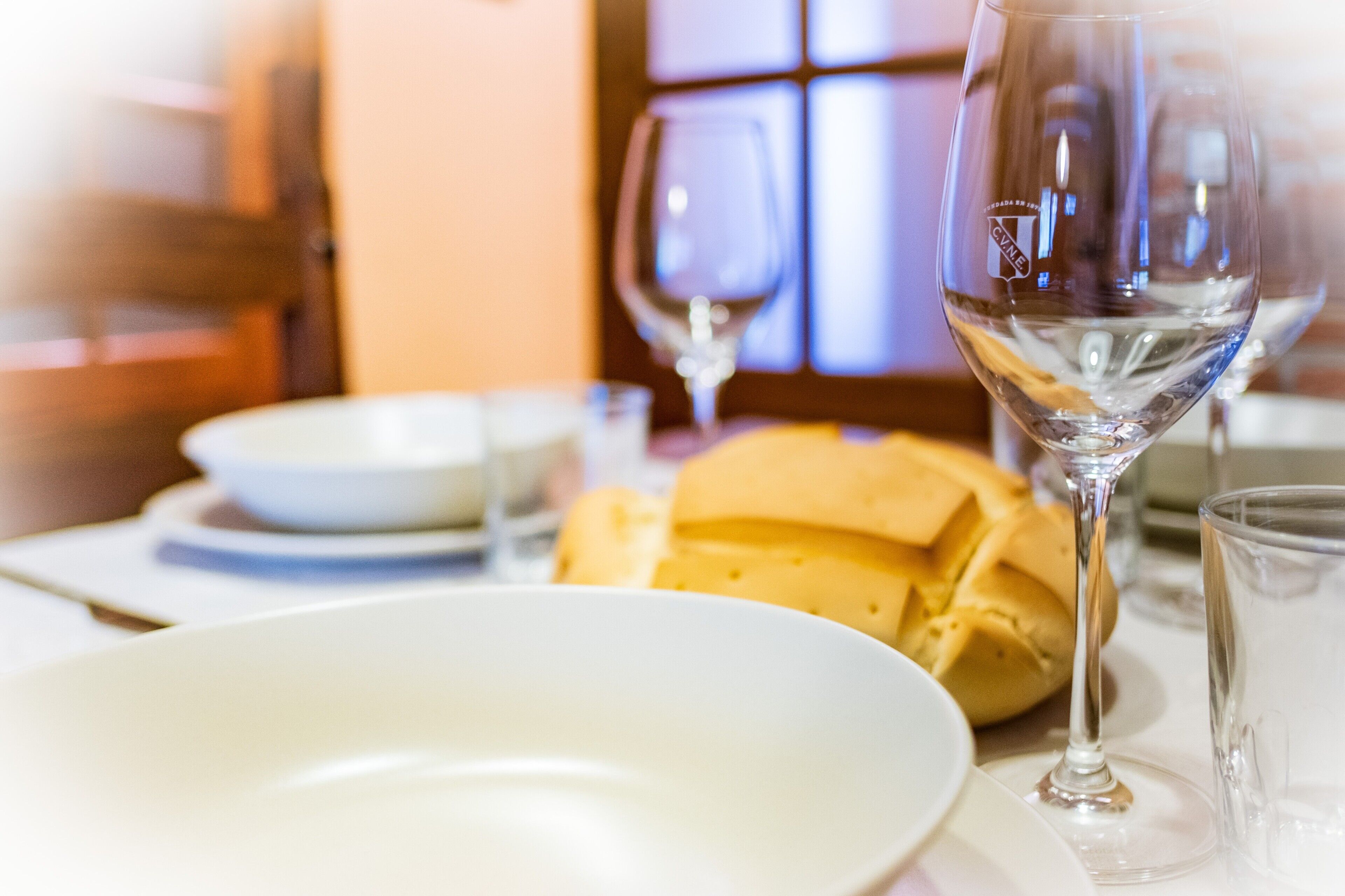 Een eettafel met een wit bord, een glas water en een brood.