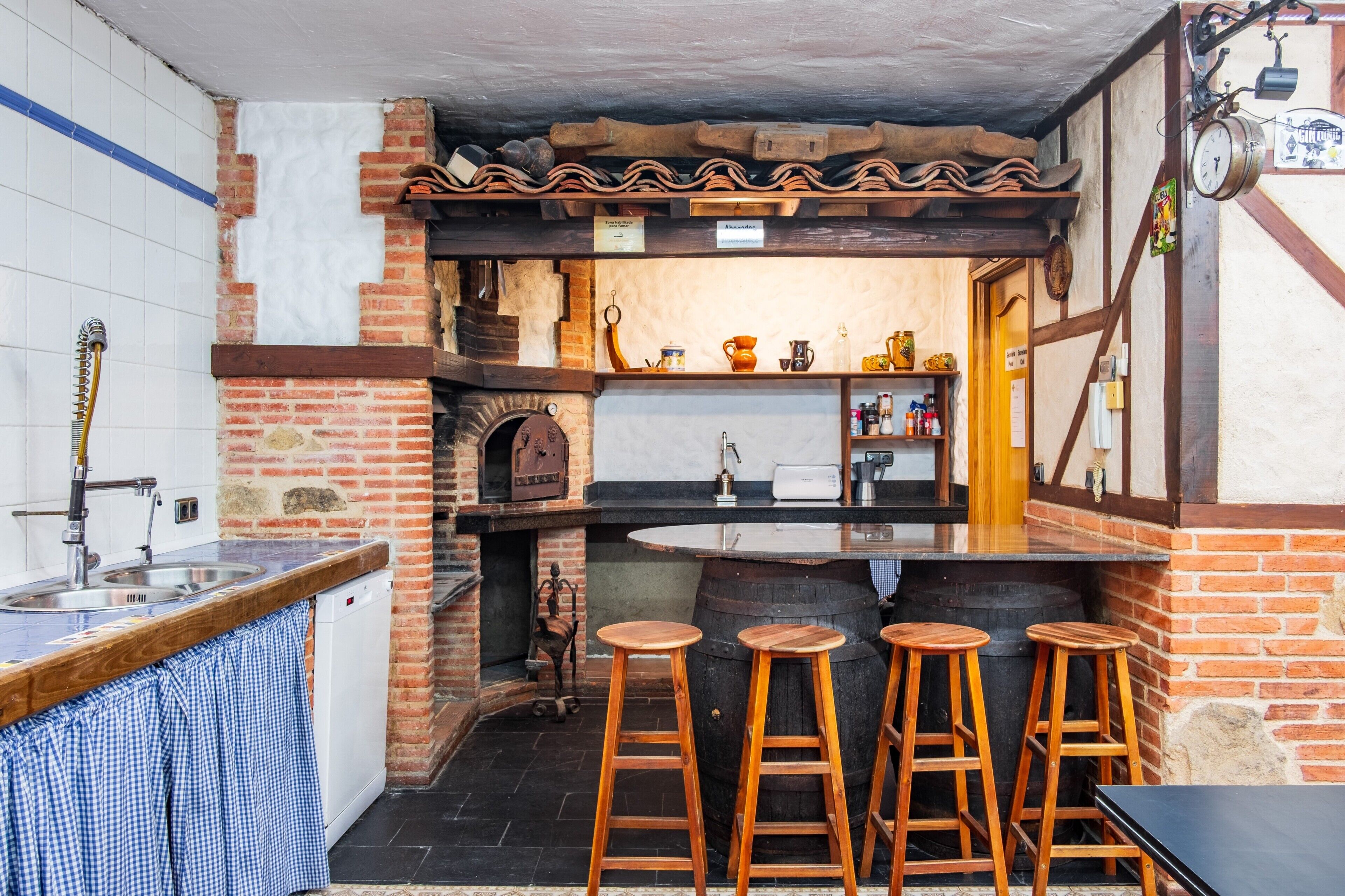 Una cocina con pared de ladrillo, taburetes de madera, un lavabo y una barra.