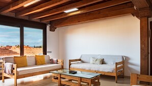 Una habitación con techo de madera, una mesa de centro de vidrio, un sofá, una cama y vistas de edificios a través de amplios ventanales.