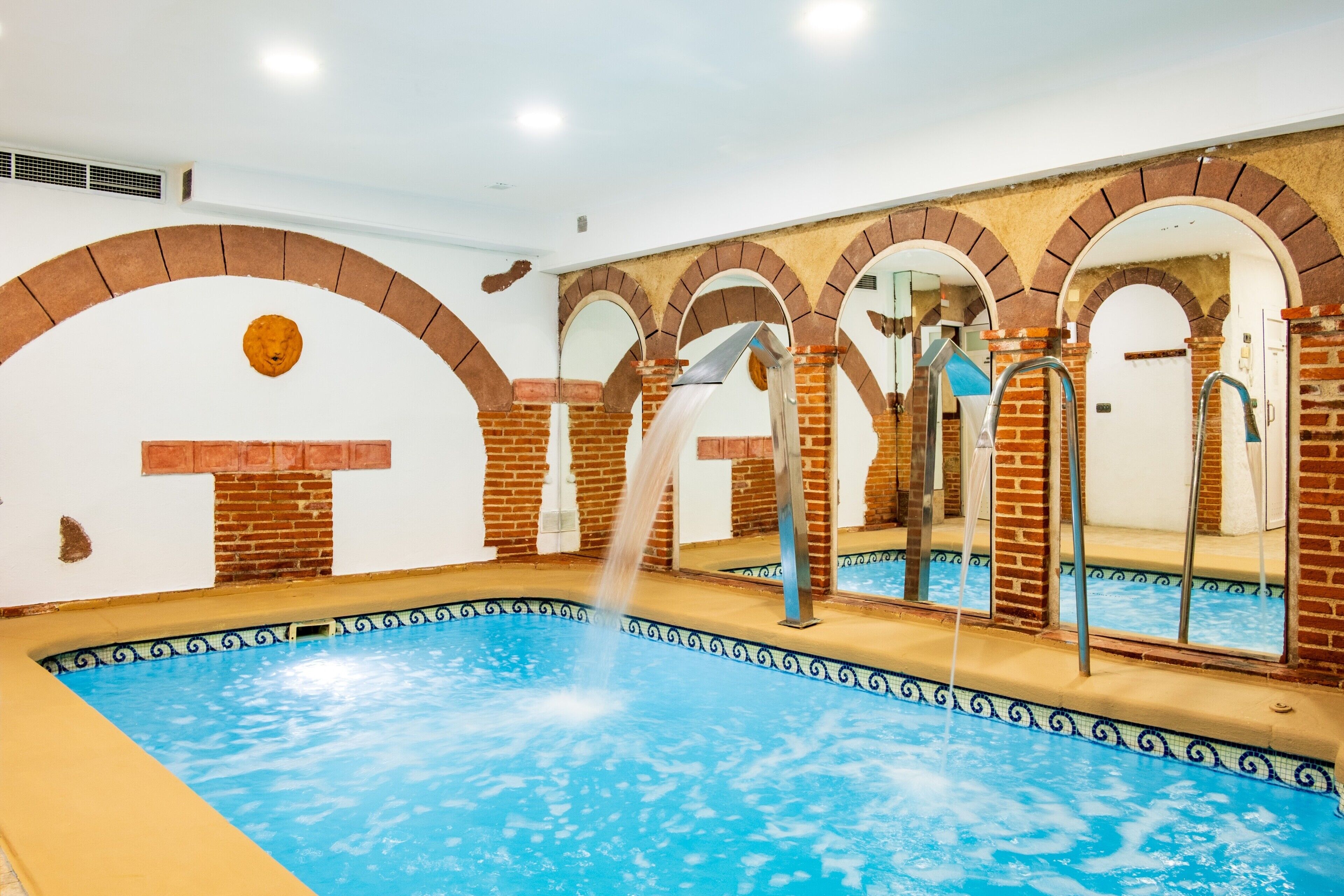 A swimming pool with a water fountain, surrounded by brick arches and a tiled border.