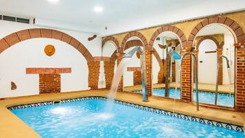 A swimming pool with a water fountain, surrounded by brick arches and a tiled border.