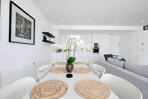 Un comedor moderno con una mesa blanca, individuales tejidos y un jarrón con flores blancas.