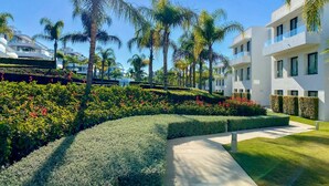 A modern hotel with a landscaped garden, palm trees, and a clear blue sky. - Luxury 2-Bed Apartment with Stunning 81 m2 Terrace & Lagoon-Style Pool (Estepona)