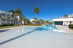 Una piscina con sillas de descanso, palmeras y edificios modernos.