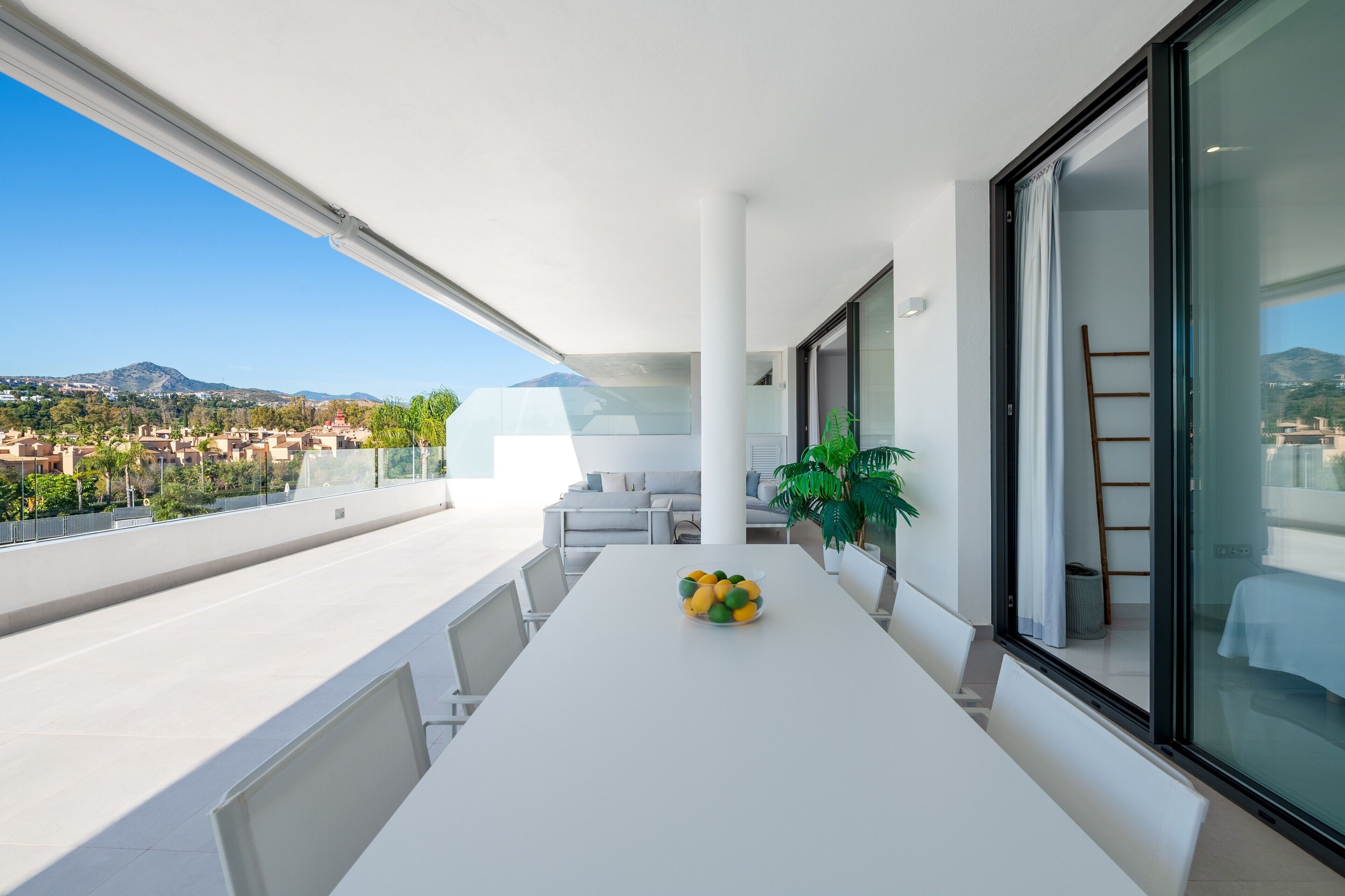 Een balkon met een witte tafel, een schaal fruit en een plant.