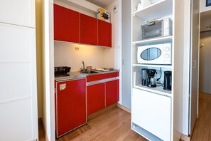 Une cuisine de taille réduite avec des placards rouges, un four à micro-ondes, une machine à café et un évier.