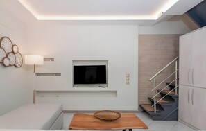 Una sala moderna con un televisor de pantalla plana, una mesa de madera con una cesta tejida, un sofá, una escalera y un estante fijado a la pared.