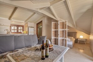 Une pièce confortable de style loft, avec un plafond haut, un canapé, une table à manger ornée de bouteilles de vin et un lit doté d’une tête de lit.