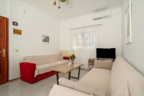 Uma sala de estar com sofá, mesa de centro, televisão e janela com cortinas.