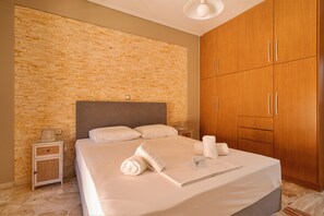 Une chambre d’hôtel avec un mur décoré d’un motif en briques, un lit avec du linge de maison blanc, une armoire en bois et une table de chevet avec une lampe.