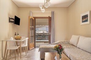 Een kamer met een bed, een eettafel met stoelen, een aan de muur bevestigde televisie en een balkon met een hekwerk.
