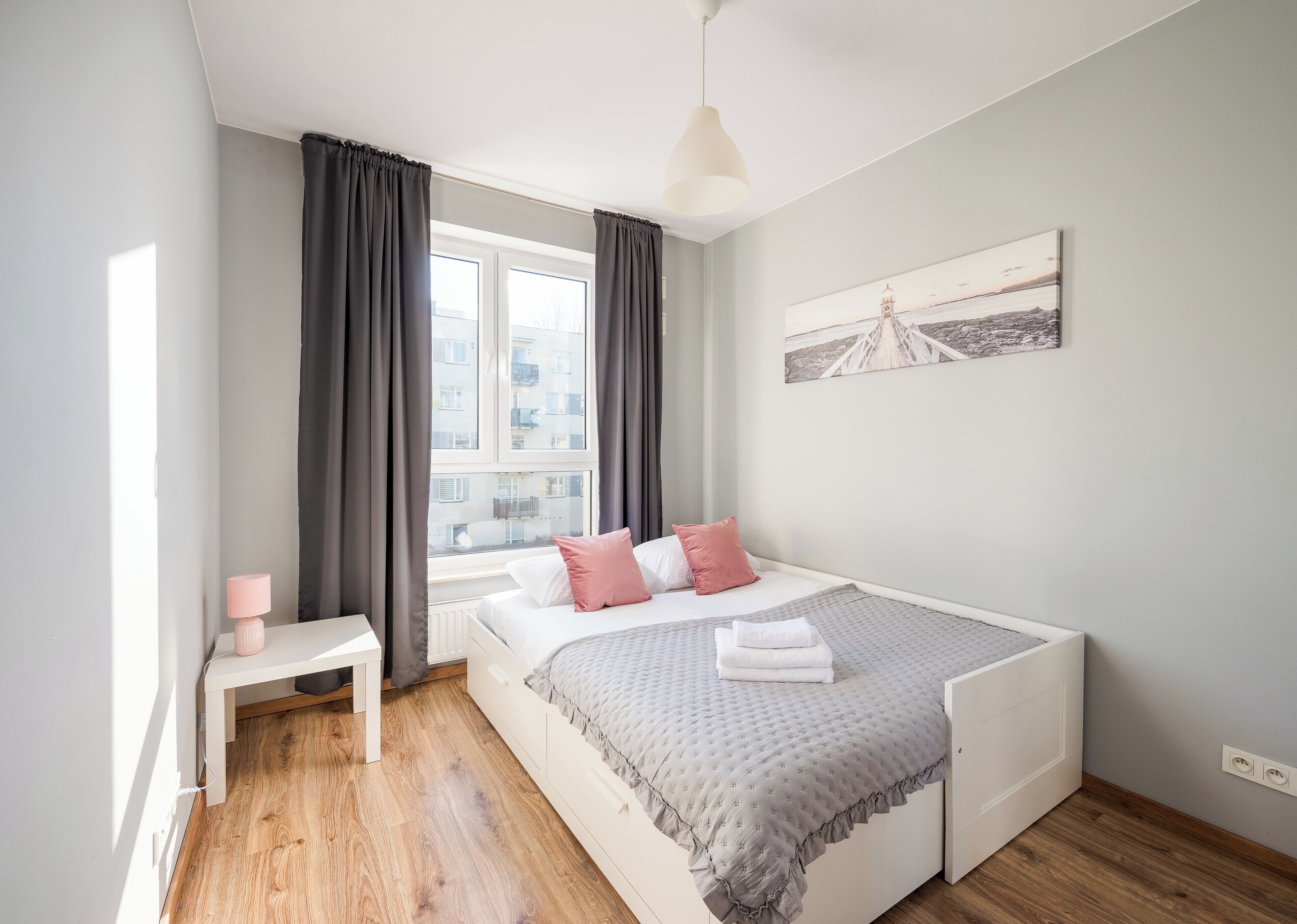 A modern bedroom with a bed, bedside table, and a window with curtains.