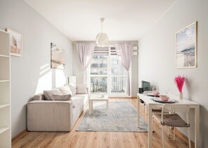 Un salon moderne avec un canapé, une table à manger et une chaise. On y trouve une fenêtre avec des rideaux, un luminaire suspendu et un vase rempli de fleurs sur la table.