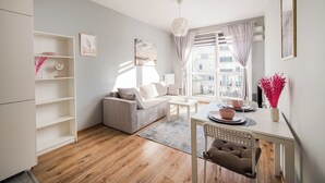 A modern living room with a sofa, a dining table, and a kitchen area with a white cabinet and shelves. - Warszawa-Włochy Serene Apartment (Warszawa)
