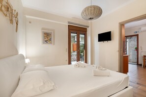 A hotel room with a bed, a television, a painting, and a door leading to a balcony. - Studio 'Assos' with Wi-Fi and Air Conditioning (Argostoli)