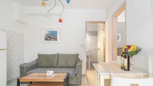 A modern living room with a sofa, a wooden coffee table, a dining table with chairs, a vase with flowers, and a framed picture on the wall. - Studio 'Ainos' with Private Terrace, Wi-Fi and Air Conditioning (Argostoli)
