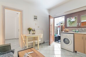 Un espace de vie compact comprenant un coin repas, un lave-linge et une vue dégagée sur l’extérieur grâce à une porte ouverte.