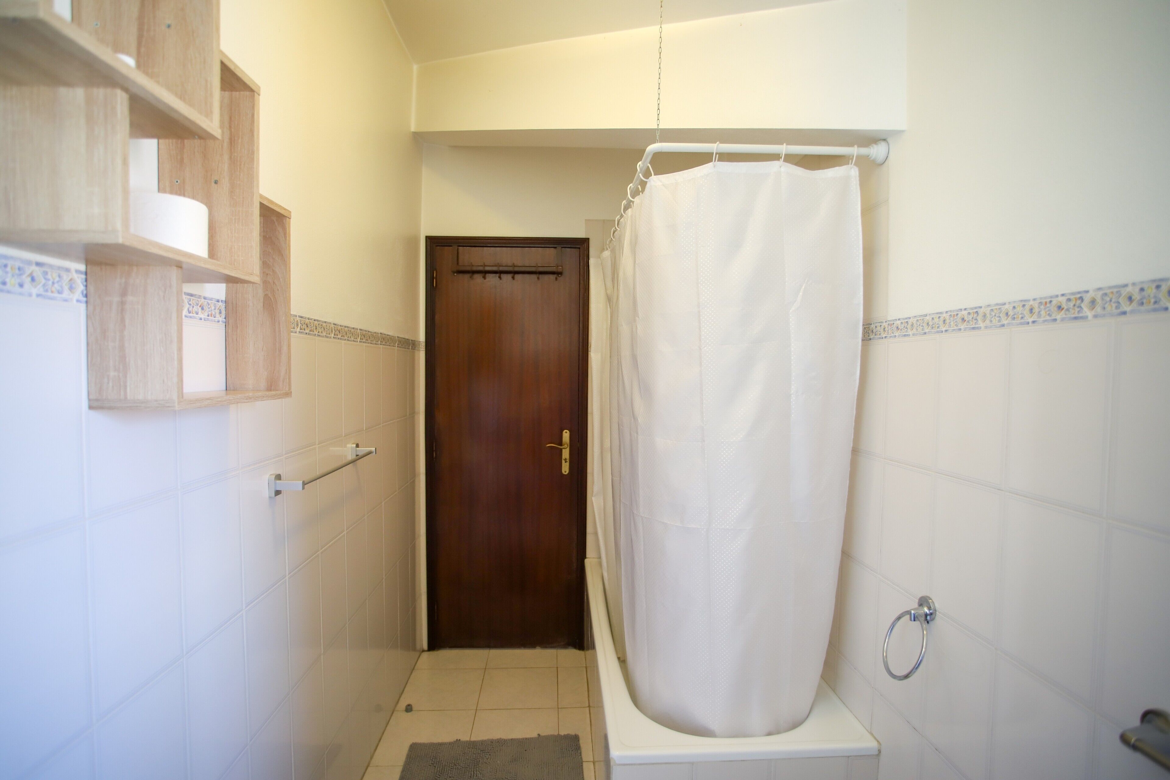 Et badeværelse med brusevæg, en trædør og en hylde med toiletartikler.