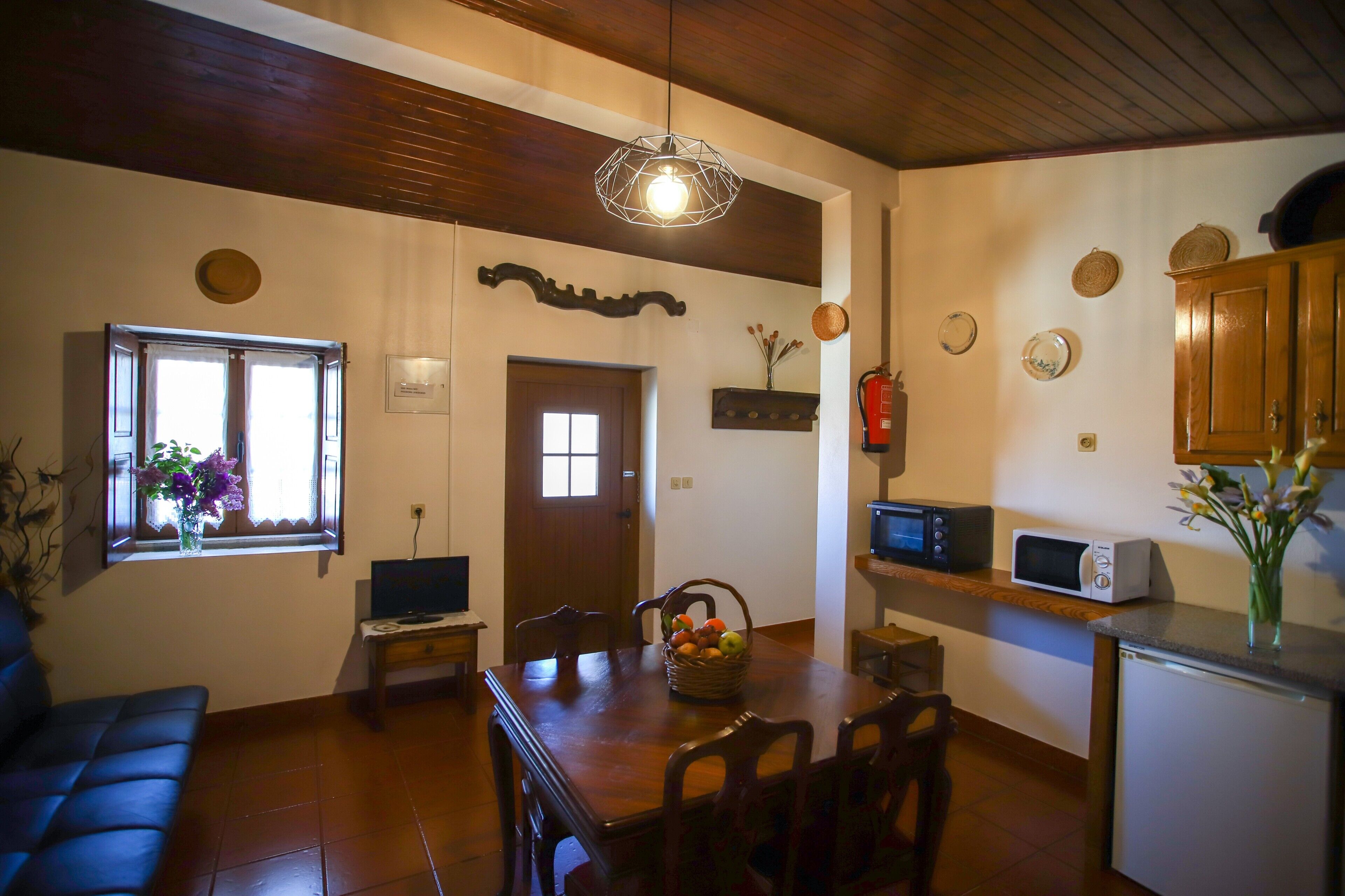 A dining area with a wooden table, chairs, a television, and a kitchen area with a microwave and cabinets.