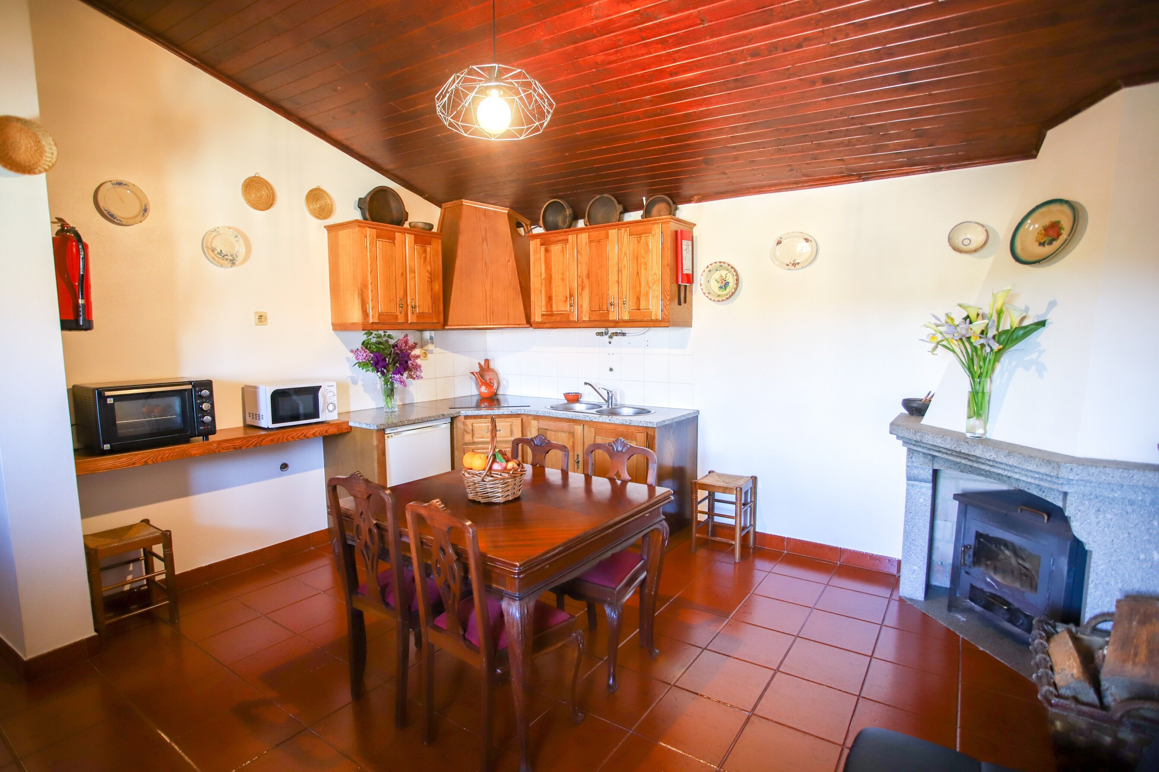 Una cocina con armarios de madera, una mesa de comedor, sillas, un microondas, un fregadero y una chimenea.
