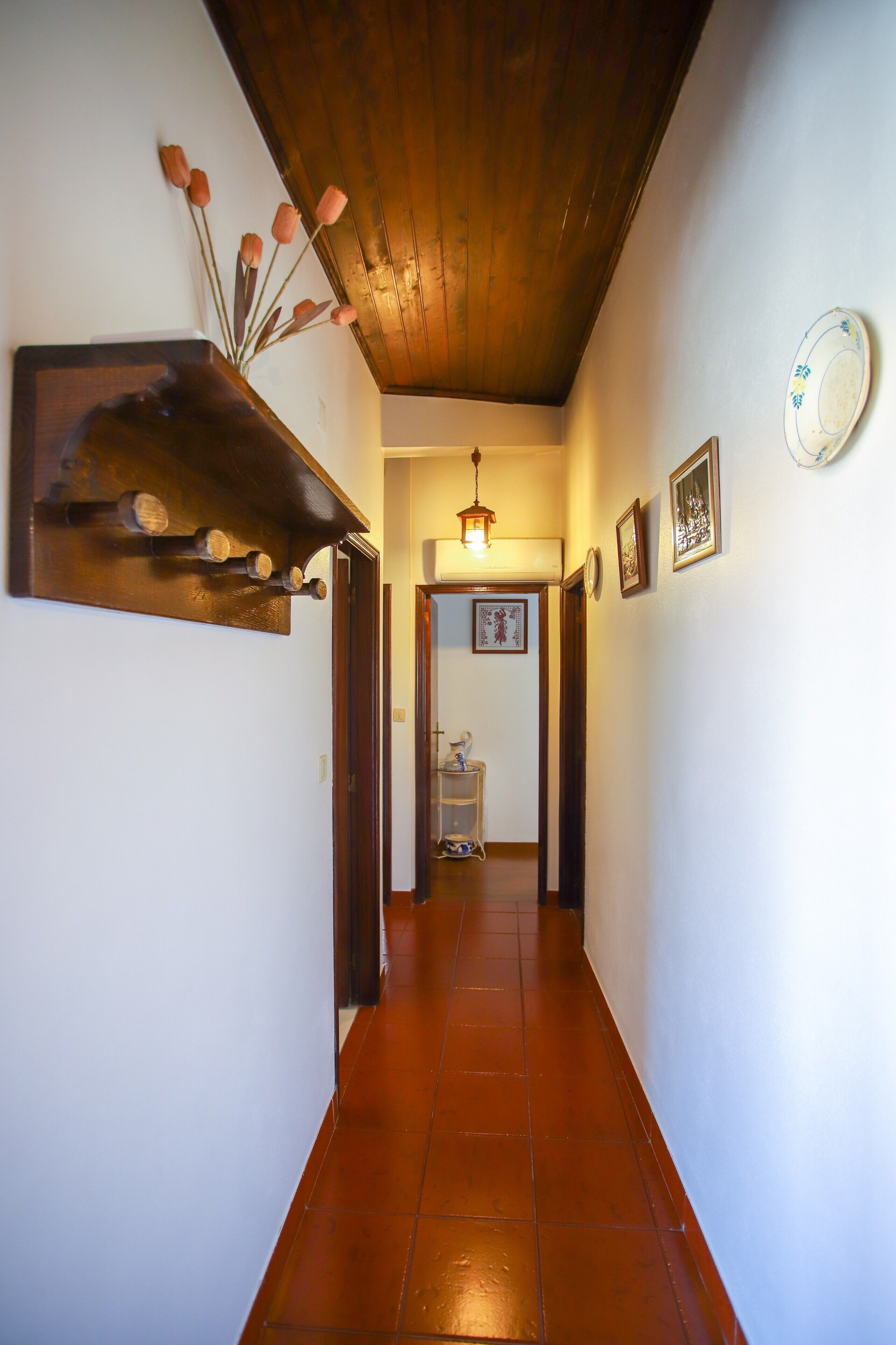 A hallway with a wooden ceiling, a wall-mounted wooden shelf, and a tiled floor.
