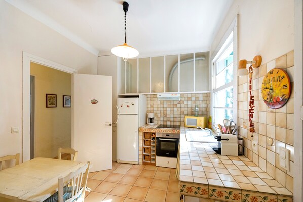 A kitchen with a refrigerator, oven, microwave, and a clock on the wall.