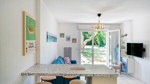 A modern kitchen with a granite countertop, bar stools, a blue sofa, and a television mounted on the wall.