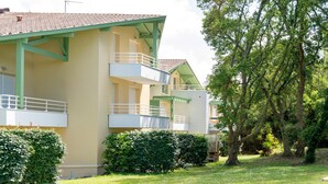A multi-story building with balconies, surrounded by greenery and trees.