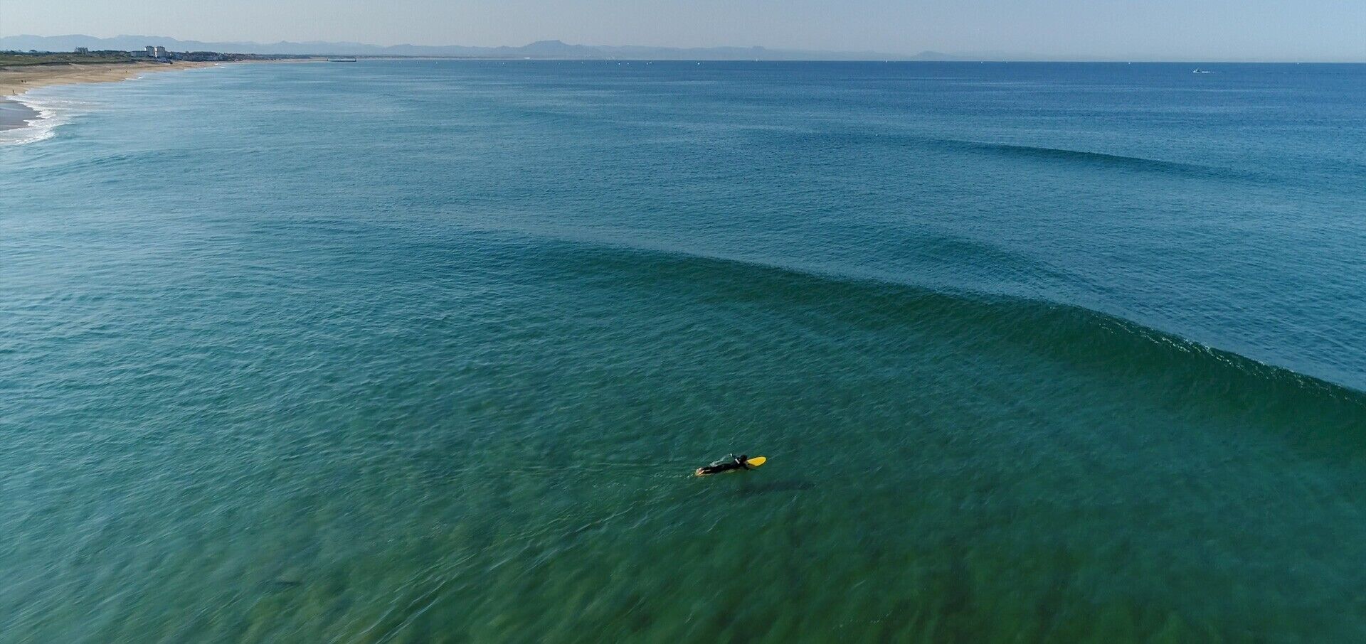 Uitzicht op de kust met helder water, een persoon die peddelt en land in de verte.