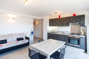 A modern kitchen with dark cabinets, a built-in oven, and a dining area with a table and chairs.