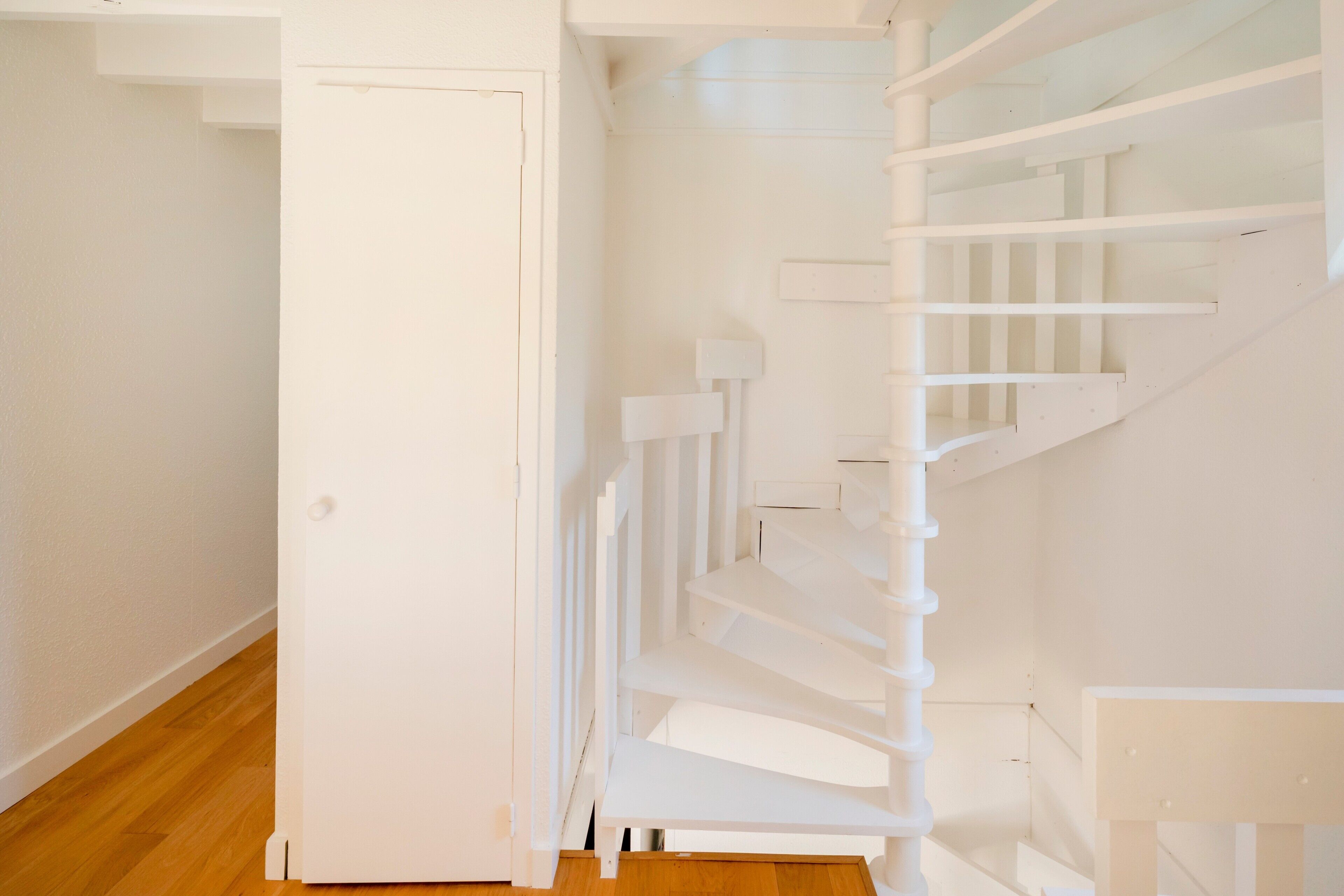 A white staircase with a wooden floor, a white door, and a white wall.