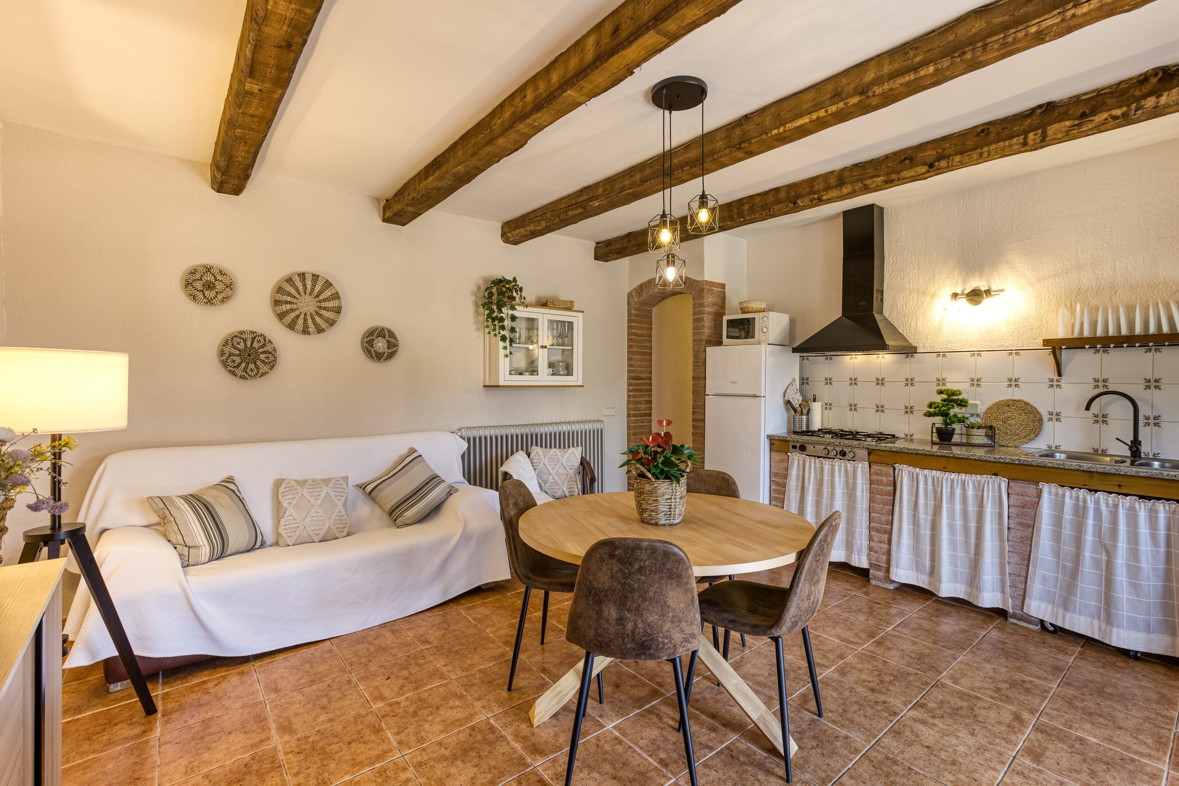 A cozy kitchen with a wooden ceiling, a dining table with chairs, a sofa, and a kitchen counter with appliances.