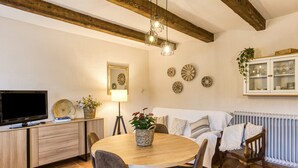 A cozy dining area with a wooden table, chairs, a television, and a cabinet with glass doors. - Country House 'Can Planas 1' with Shared Pool, Wi-Fi and Air Conditioning (Fonolleres)