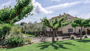 A courtyard with a table and chairs, a bench, and a building with a tiled roof. - Country House 'Can Planas 1' with Shared Pool, Wi-Fi and Air Conditioning (Fonolleres)