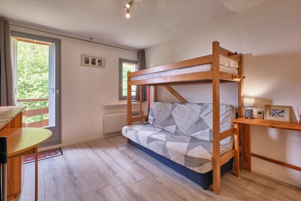 Ein Stockbett mit gemustertem Lattenrost, ein Holztisch und ein Fenster mit Blick auf Grünflächen.
