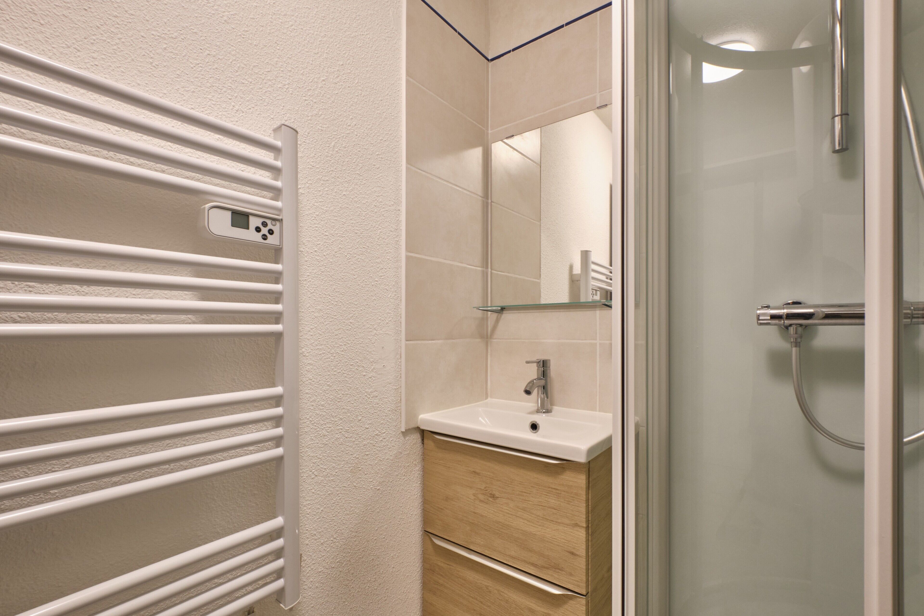 A modern bathroom with a glass shower enclosure, a white sink, and a towel rack.