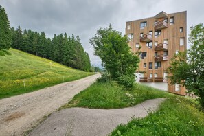 Ein modernes Gebäude mit mehreren Balkonen, umgeben von Grünpflanzen und einem Feldweg.