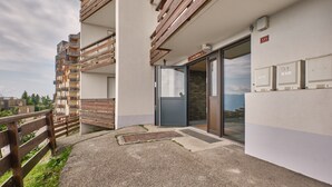 Un edificio moderno con un balcón de madera, una puerta con panel de vidrio y vistas a la montaña.