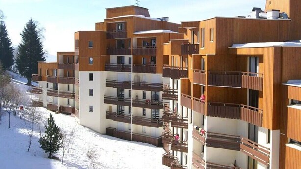 Un edificio de varios pisos con balcones, techo plano y suelo cubierto de nieve.