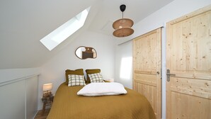Een slaapkamer met een bed, een houten garderobe, een spiegel, een lamp en dakraam.