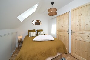 Un dormitorio con cama, armario de madera, espejo, lámpara y tragaluz.