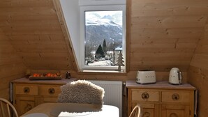 Een knus slaapkamer op zolder met een houten schuine dak, een raam met uitzicht op besneeuwde bergen, een houten dressoir en een radiator.