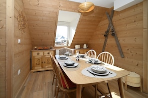 A wooden dining room with a sloped ceiling, a wooden cabinet, and a dining table set with plates, glasses, and cutlery. - Ideal Getaway at Lake Loudenvielle – Comfortable Apartment with Outdoor Activities (Genos)